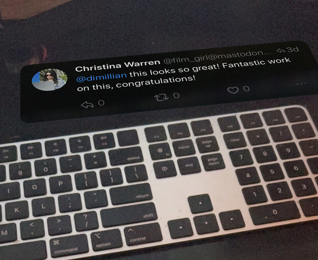 A virtual Mastodon post "flat on a desk" in AR with a Mac keyboard in the real world below it.