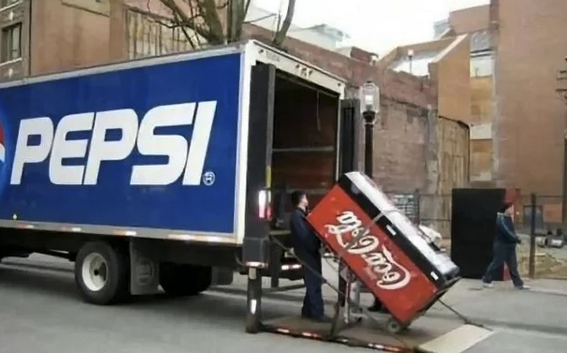 Worker loading a Coke vending machine into the back of a trailer that has "Pepsi" logo on it.