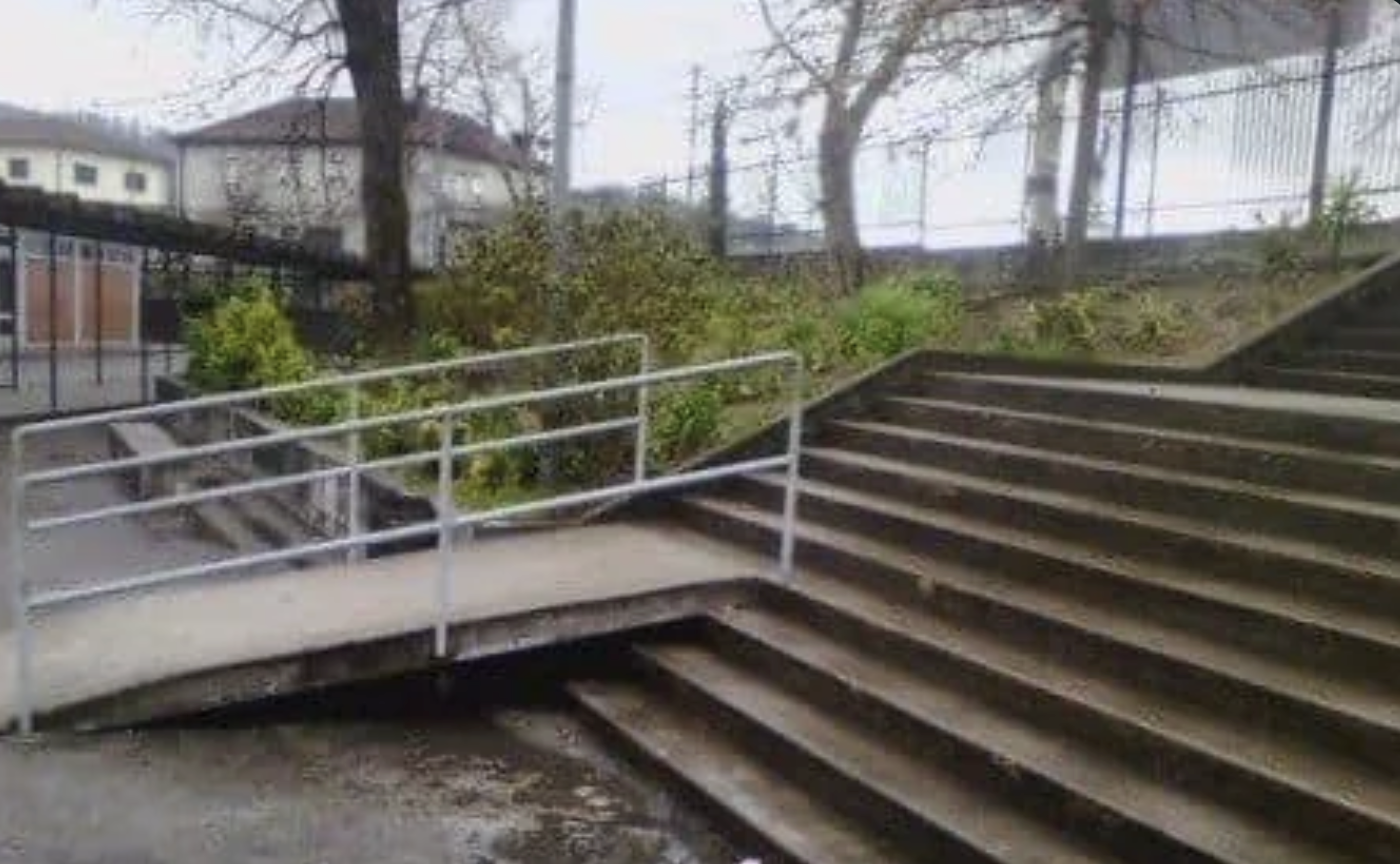 Outside a flight of stairs, with a ramp (with handrails) built that goes from the ground floor to the fourth step from the bottom, requiring anyone using the ramp to still go up majority of the stairs.