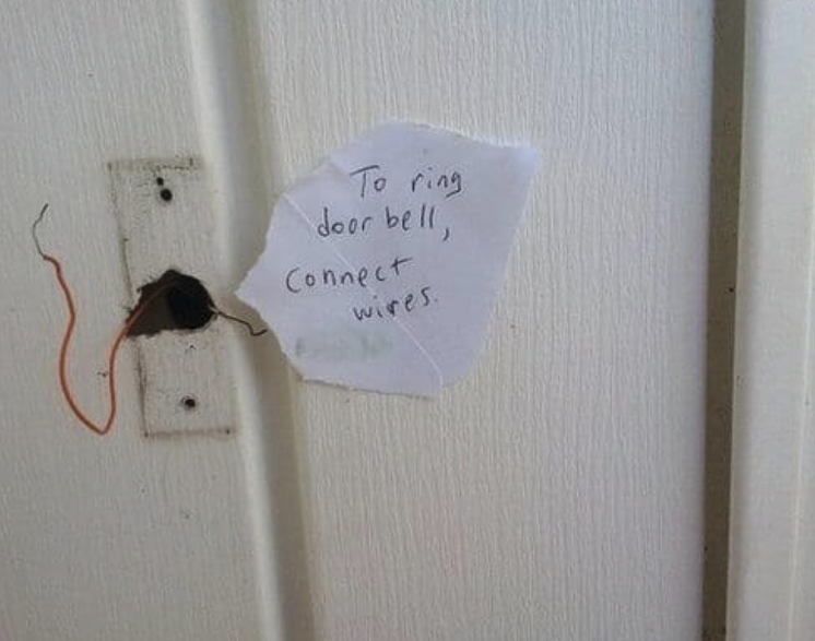 A hand written note that says "To ring door bell, connect wires" taped next to a small hole in the wall with two electrical wires, currently not touching.