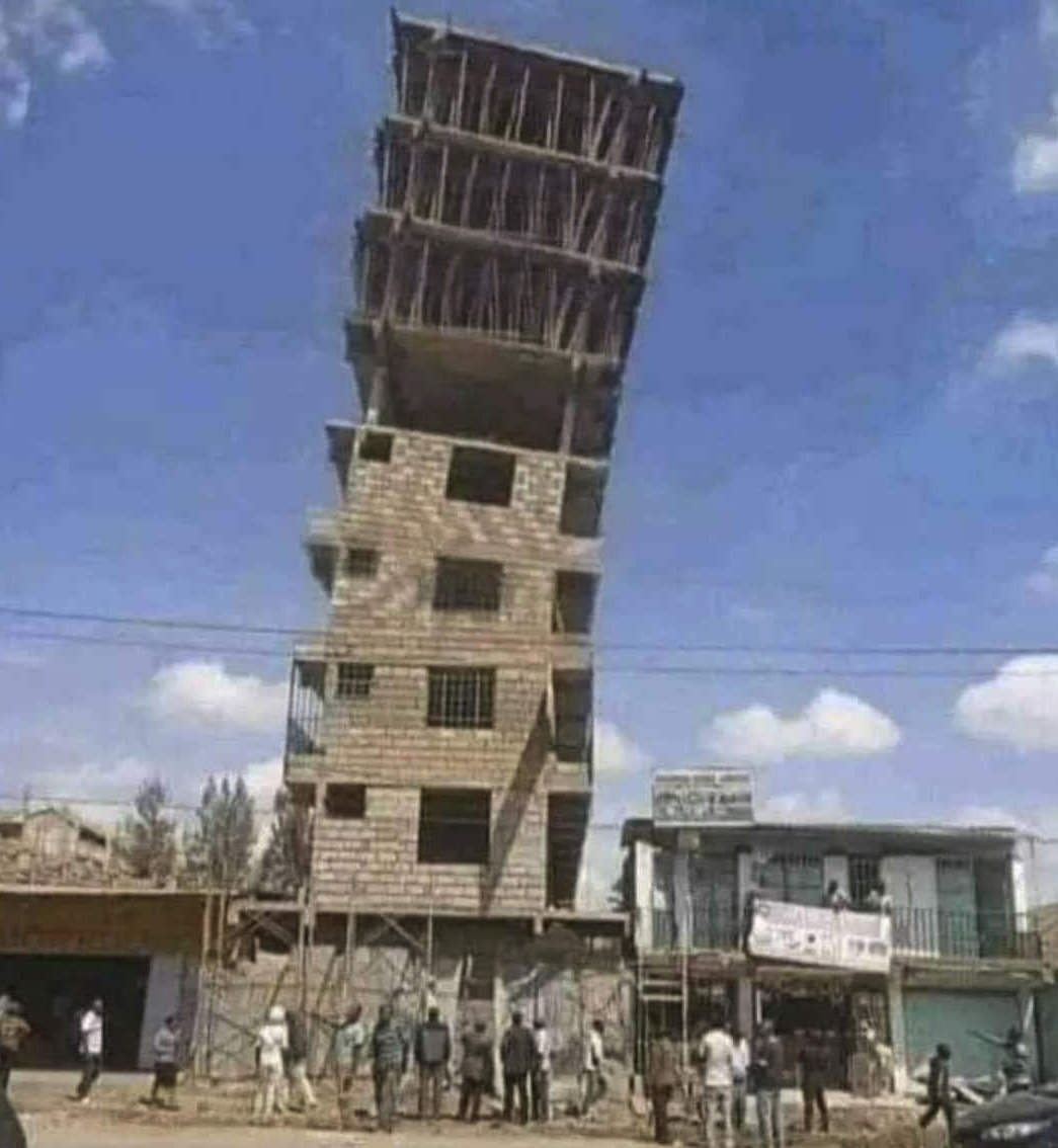 An eight story brick building that is leaning toward the right and whose's top 4 floors are obviously not completed, missing walls.