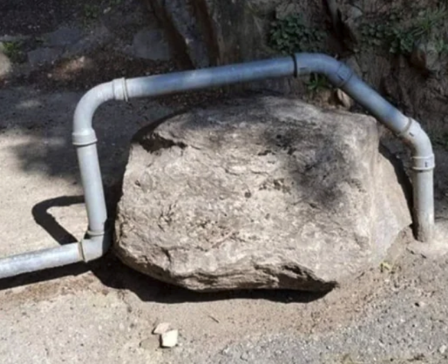 Outdoors - a water pipe that is going above a decently sized (but easily movable?) rock.