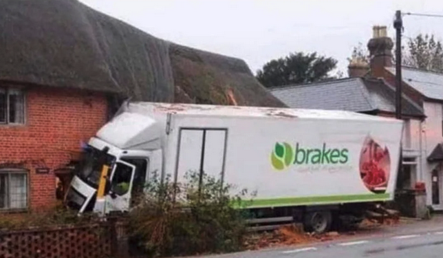 A truck that has crashed into the side of a brick house with the word/logo "brakes" on the side of it.