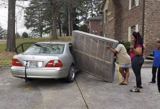 three people attempting to put a large mattress into a 4 door sadan and they can't even get one of the corners past the open rear passenger door.