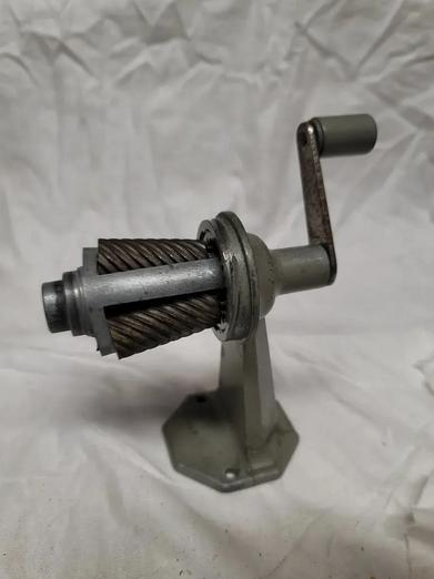 An old fashioned grey-colored metal hand cranked pencil sharpener that could be attached to a wall or desk.