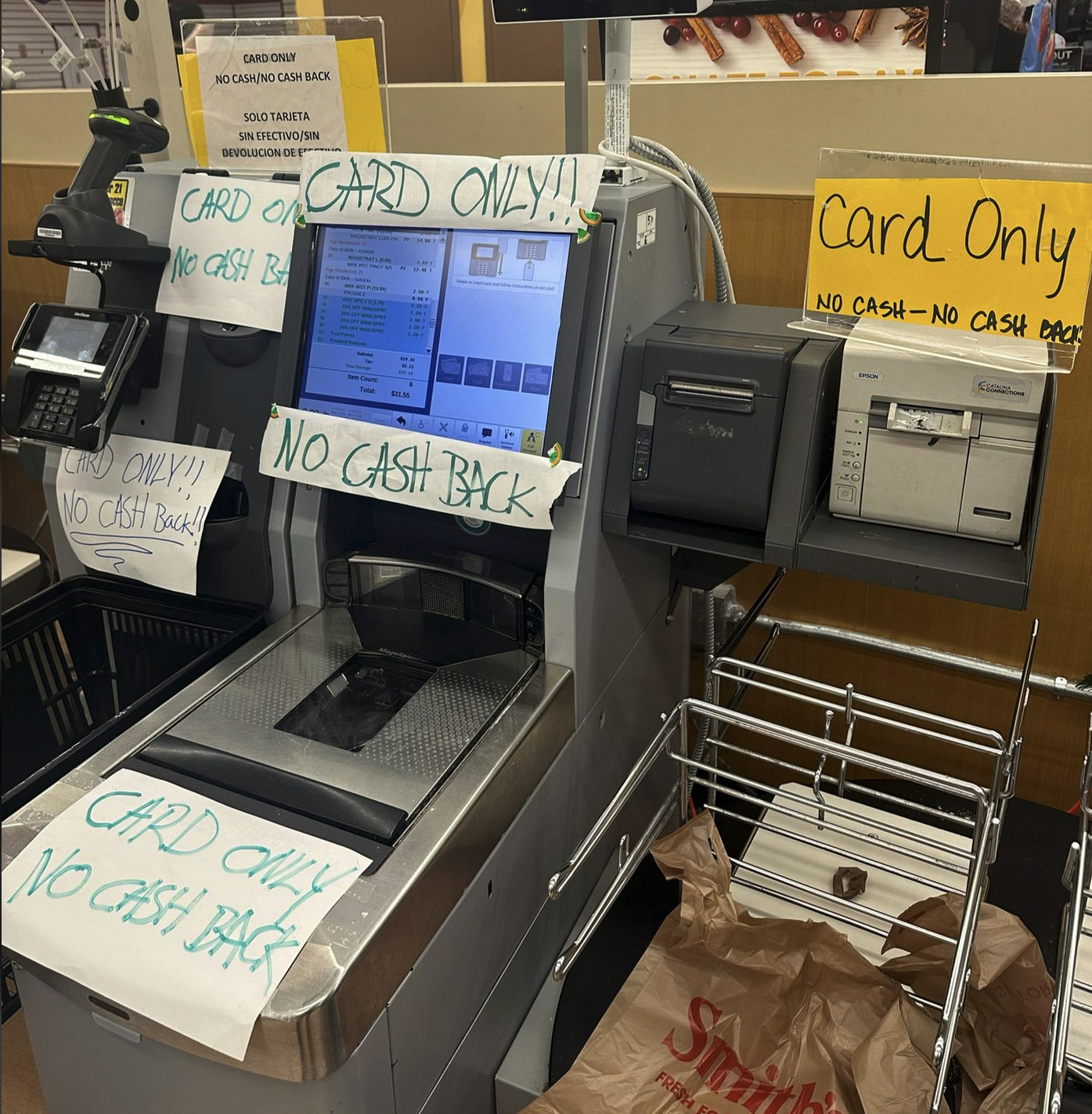 a self checkout center at a store that has a million "CARD ONLY NO CASH BACK" signs around/on it.