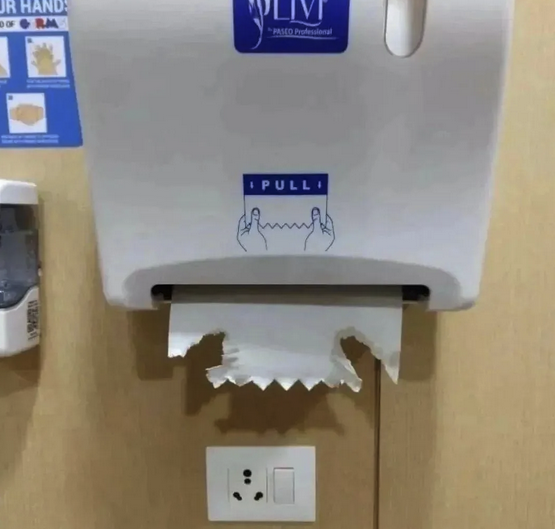 Paper towel dispenser with instructions to use two hands to pull down the next dispensed sheet. Someone tried but ripped their fingers through it.