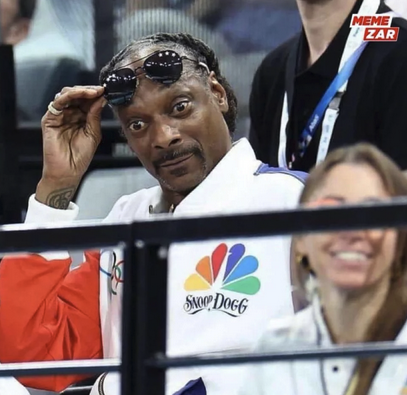 Snoop Dogg at the 2024 Olympics looking pleasurably surprised raising his sunglasses.