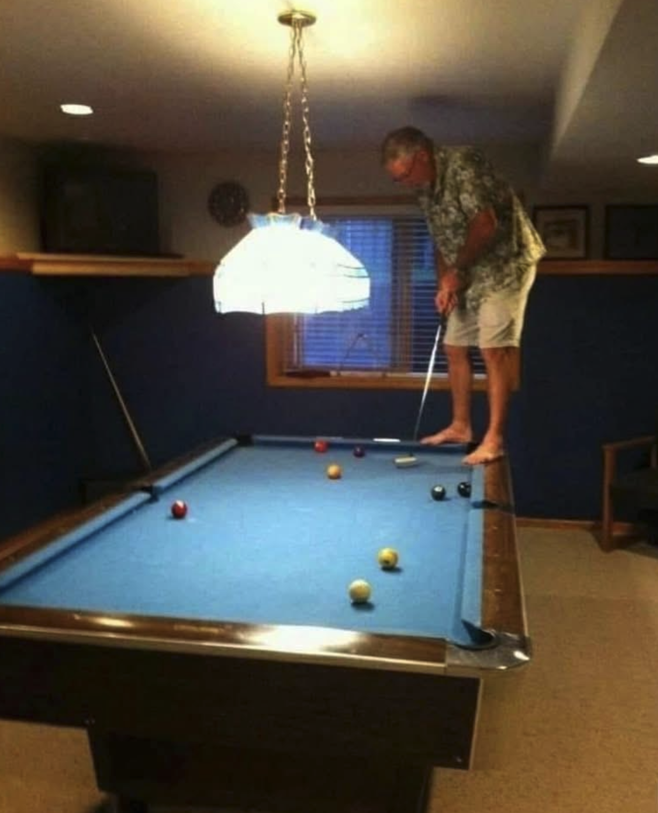 Man on top of pool table with golf club.