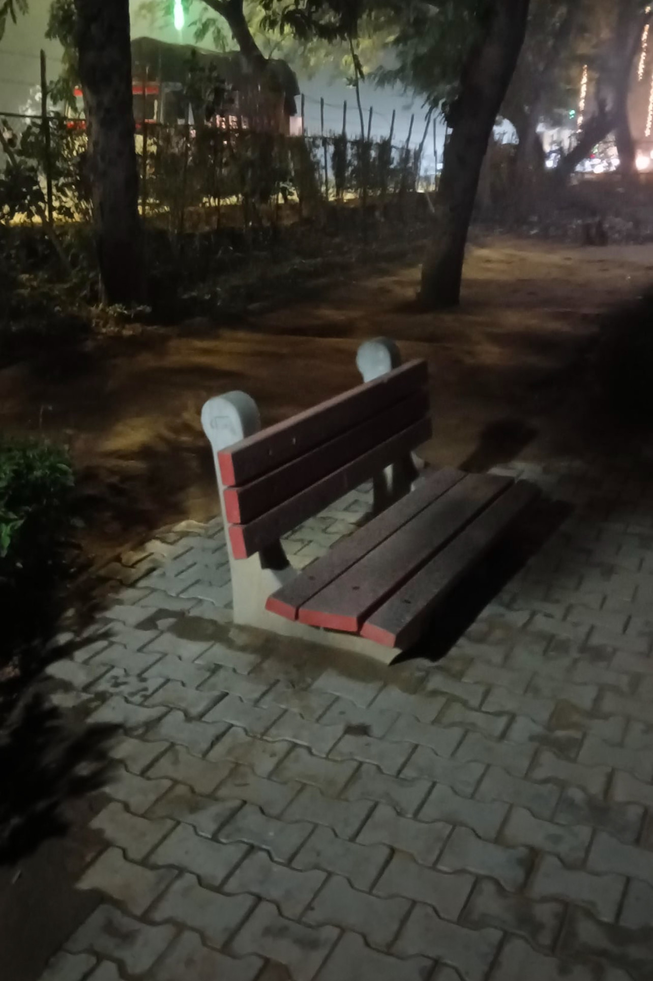 An evening picture of a bench in a park. The bench appears sunken into the brick floor.