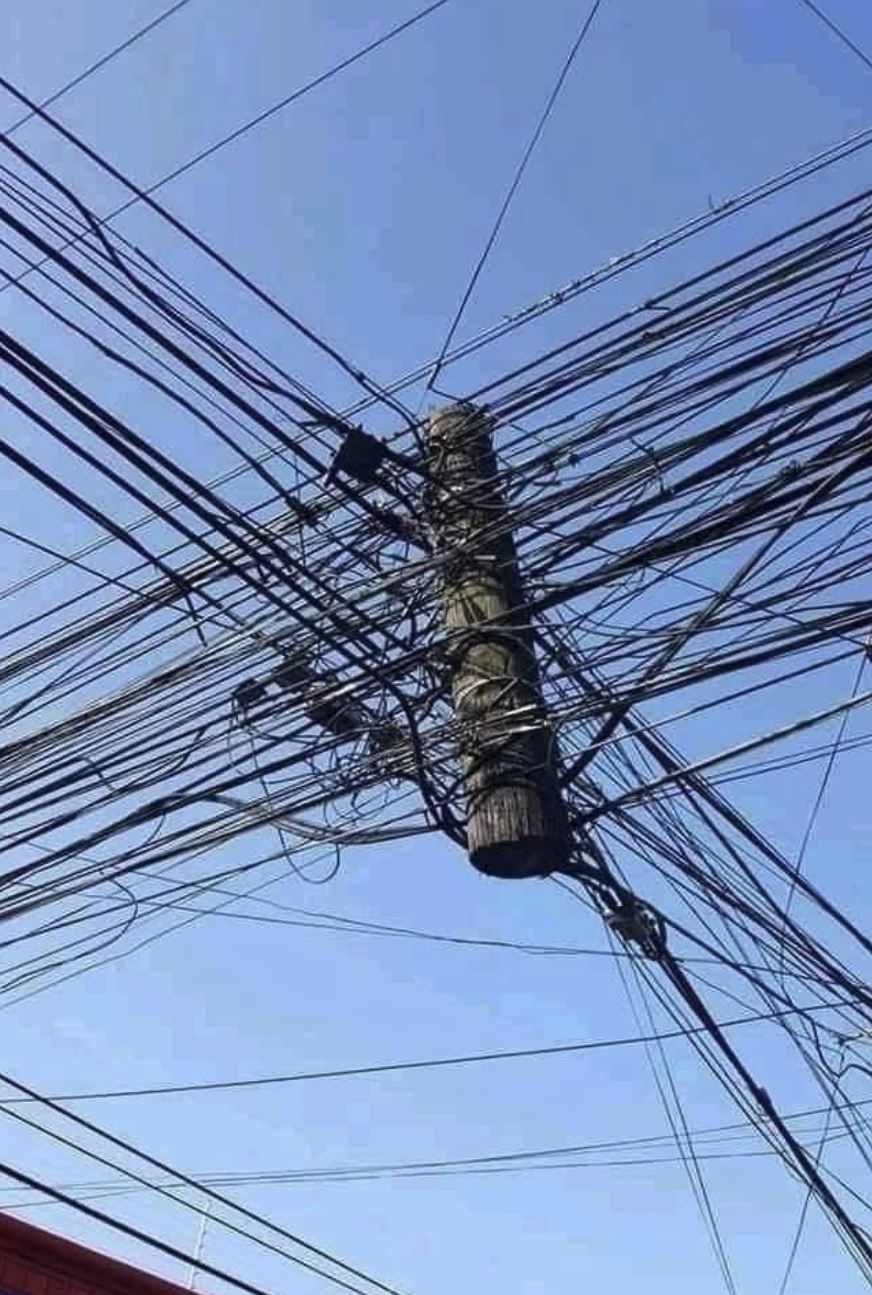 tons of telephone or power wires intersecting at the top part of disconnected telephone pole.