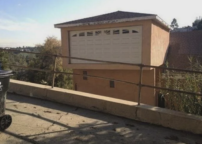 View of a two-story house but the garage door (closed) is on the second story and what looks to be a regular wall/windows is on the first story.